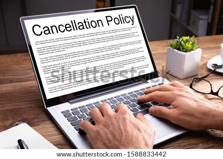 Man Reading Agreement Of Cancellation Policy On Laptop Screen Over Wooden Desk At Office