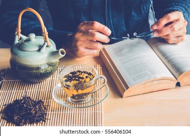 A Man Reading A Book With Cup Of Tea And Tea Pot