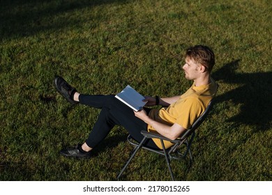 Man Reading A Book In Garden Recliner Chair. Summer Vacation In The Yard Garden. Scandinavian Male Life In Holidays. Good Living. View From The Top. Beautiful Young Man Resting. Daily Simple Life