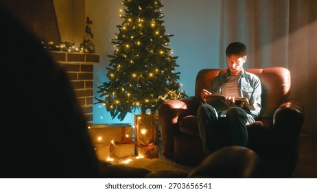 Man Reading a Book While Sitting on the Sofa at Christmas Near the Tree