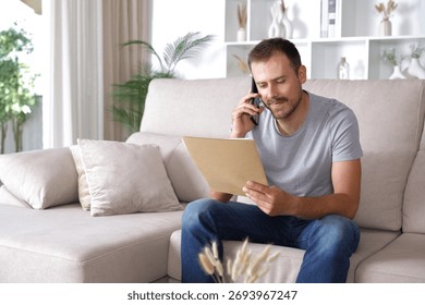 Man reading document and consulting talking on phone sitting on a couch at home