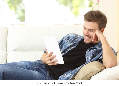 Man Reading An Ebook Or Tablet Sitting On A Comfortable Couch At Home