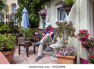 Man Reading Magazine In Home Garden, Front Door 