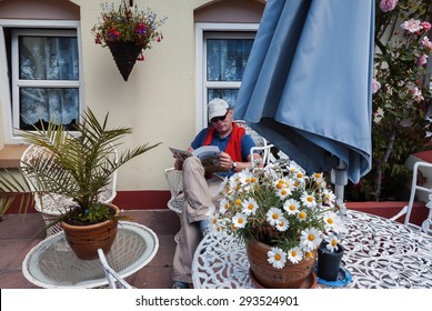 Man Reading Magazine In Home Garden, Front Door 