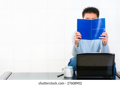 Man Reading Manual Book In Front Of His Laptop