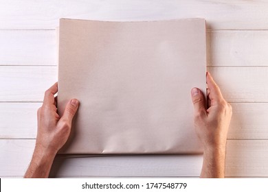 Man Reading Newspaper on White Wooden Background. Top View of a Man's Hands Holding a Blank Newspaper next to a Cup of Coffee, a Calculator and a Pencil. Copy Space for your text and image.