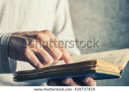 Man reading old book with torn pages, close up of adult male hands