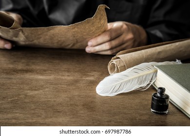 Man reading an old letter. Old quill pen, book and papyrus scroll on the wooden table. Historical atmosphere.