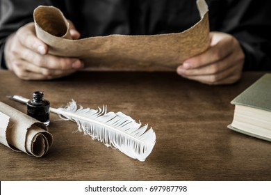 Man Reading An Old Letter. Old Quill Pen, Book And Papyrus Scroll On The Wooden Table. Historical Atmosphere.