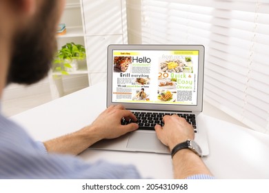 Man Reading Online Magazine On Laptop At White Table, Closeup