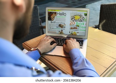 Man Reading Online Magazine On Laptop At Wooden Table, Closeup