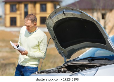 Man Reads The Manual Near The Car With The Hood Open