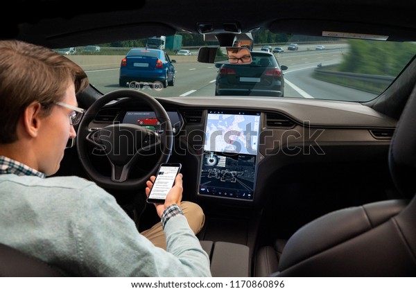 A man reads news\
online in a smartphone while his car is driven by an autopilot.\
Self driving vehicle concept