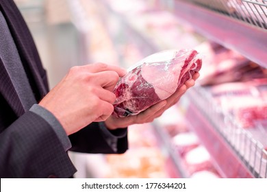 A Man Reads Product Information, Stands Near The Refrigerator In A Supermarket In The Meat Department