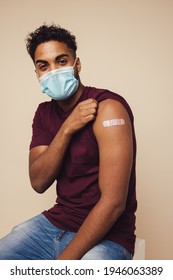 Man Receiving A Covid Vaccine. Man Wearing Protective Face Mask Showing His Arm After Getting Vaccine Shot On Brown Background.