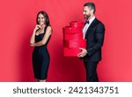 Man receiving present. Happy Valentines day. Couple in love isolated on red. Birthday couple with gift. Loving man giving present gift box for Valentines day to surprised woman. Commemorative moment