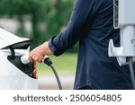 Man recharging battery for electric car during road trip travel EV car in natural forest or national park. Eco friendly travel during vacation and holiday. Exalt