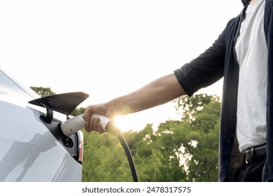 Man recharging battery for electric car during road trip travel EV car in natural forest or national park with sunrise lighting. Eco friendly travel during vacation and holiday. Exalt - Powered by Shutterstock