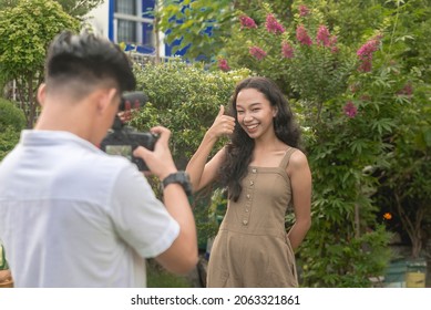 A Man Records A Vlog Of His Friend With A DSLR. A Teenage Woman Making A Thumbs Up For The Introduction Video.