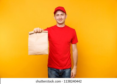 Man In Red Cap, T-shirt Giving Fast Food Order Isolated On Yellow Background. Male Employee Courier Hold Empty Paper Packet With Food. Products Delivery From Shop Or Restaurant To Home. Copy Space