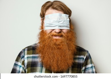 A man with a red hair and a red beard wearing a face mask over his eyes.  A bearded man with a protective mask worn in a funny way. Go crazy in the quarantine .