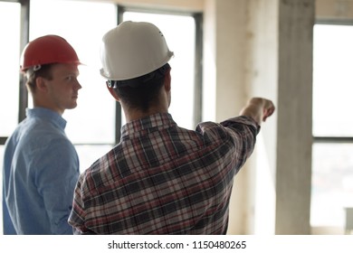 man in red hardhat is offering houses to a client. back view photo - Shutterstock ID 1150480265