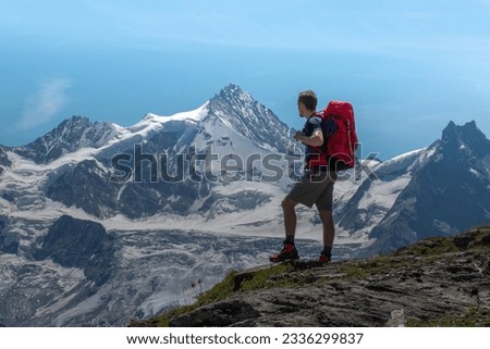 Man with a red hiking bagpack looking in the distance at the snowy swiss alps mountains