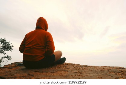 man in red hoodie sitting meditation on mountain top viewpoint sunset cloudy sky background