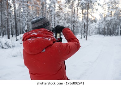 A man in a red jacket with a camera in rukh takes pictures of a winter forest