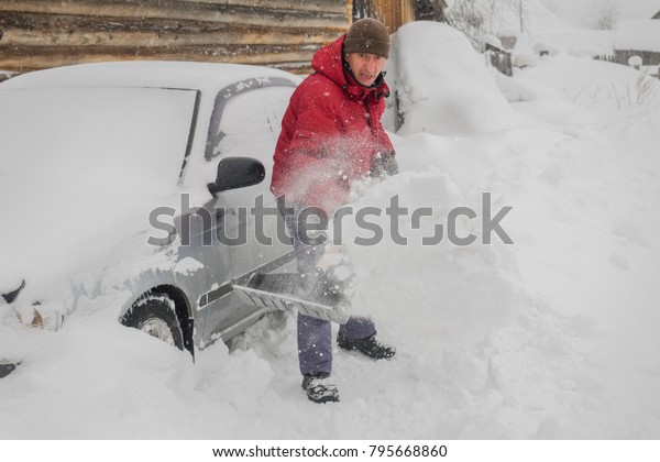 man in red jacket cleans black shovel snow\
near his car because it snowed a\
lot