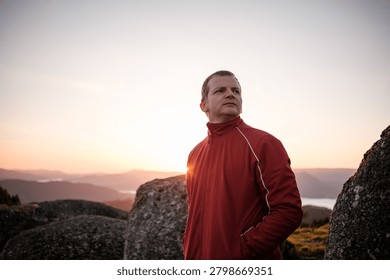Man in a red jacket looking out over a mountain landscape during sunset