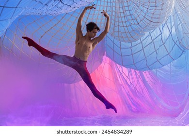 A man in red pants is doing a dance in the air. The image has a dreamy, ethereal quality to it, with the man's red pants contrasting against the blue background. Scene is one of grace - Powered by Shutterstock