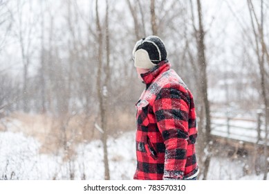Man in red plaid walking through woods on a snowy day
