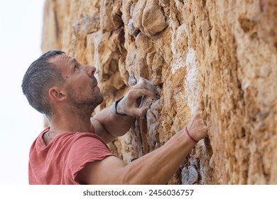 A man in a red shirt is climbing a rock wall - Powered by Shutterstock