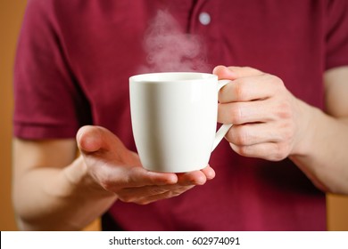 The man in the red shirt shows a clean white Cup. Cup for your design. Empty mug - Shutterstock ID 602974091