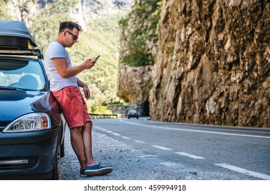 Man in red shorts standing by the Broke Down car and calling for help with smart phone - Powered by Shutterstock