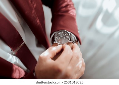 A man in a red suit is wearing a watch and adjusting it. The watch is silver and has a black face. The man is wearing a tie and a jacket, and he is in a professional setting - Powered by Shutterstock