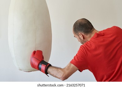 Man in red t-shirt hitting uppercut to heavy bag in boxing training