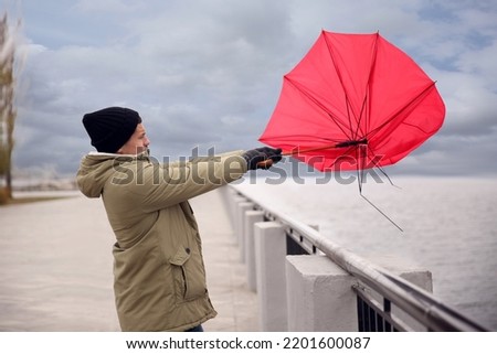 Man with red umbrella caught in gust of wind near river