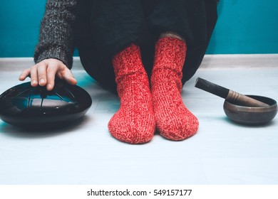 Man in a red woolen socks sitting on the floor in the yoga studio with a singing bowl and steel tongue drum - Shutterstock ID 549157177