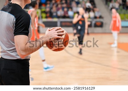 Man referee keeps the ball during basketball match. In the background players.