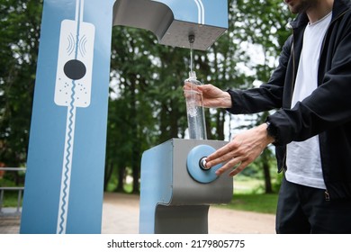 Man refilling his water bottle at the city. Free public water bottle refill station. Sustainable and green city. Male in black coat. Tap water to reduce plastic bottle usage. Drinking water dispenser