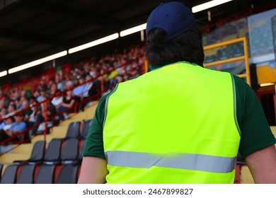 Man with reflective jacket while checking the audience in the stands of the packed stadium during the event