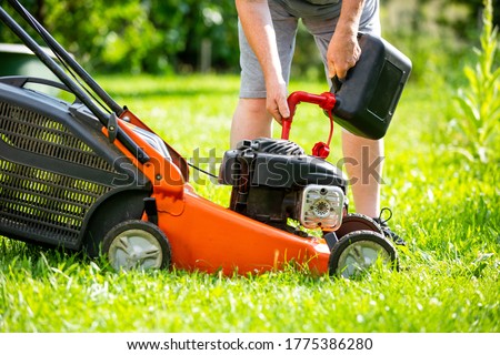 Man refueling the lawnmower on his huge garden, gardening concept