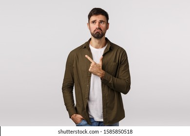 Man Regret Missed Good Opportunity Feeling Sad And Miserable. Upset Young Bearded Guy Pulling Gloomy Face, Frowning And Look Depressed, Pointing Upper Left Corner, Standing White Background