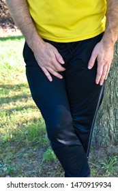 Man In Relaxed Athletic Clothes Yellow Black Holding His Itchy Crotch Leaning Against A Tree Outdoors Background