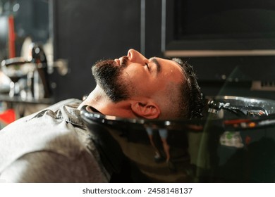 A man relaxes during a professional beard wash at a modern barbershop, highlighting meticulous grooming and personal care practices. - Powered by Shutterstock