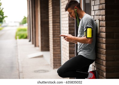 Man relaxing after jogging.He using his smart phone and listening to music.Using application and standing against the wall.