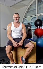 Man Relaxing After Work Out On Chair, Inside Room Of A Luxury Gym, Heavy Exercise Tools Near Wall, A Body Builder Sitting On A Bench.