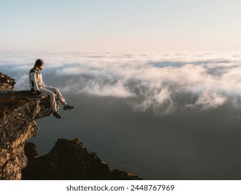 Man relaxing alone on the edge of mountain cliff in Norway above clouds and sea, traveler hiking outdoor active healthy lifestyle adventure extreme summer vacations  - Powered by Shutterstock